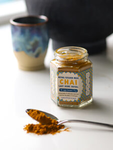 An open jar of Banging' Chai tea powder and a spoonful spilling onto the counter beside.